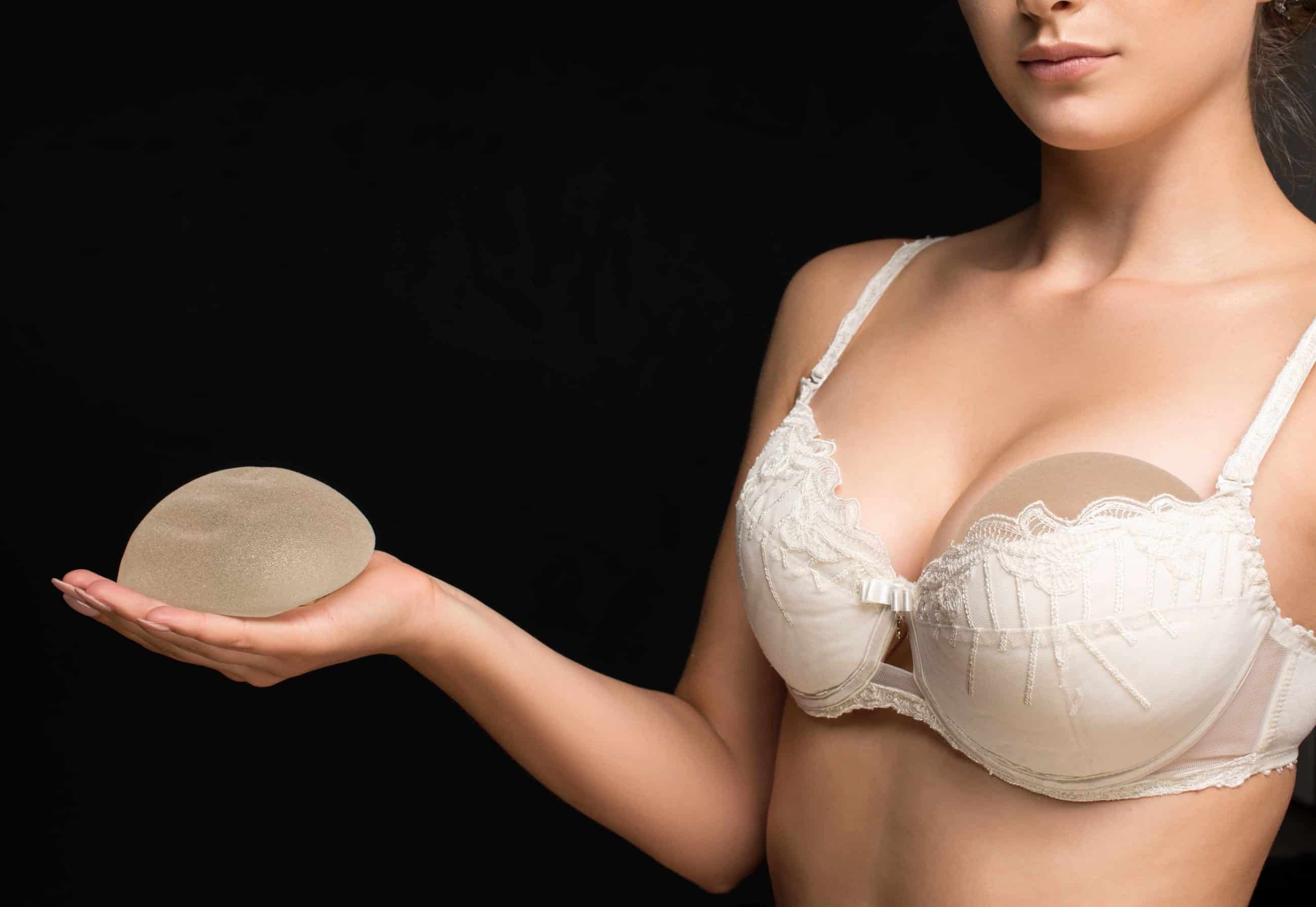 woman in white bra holding breast implants